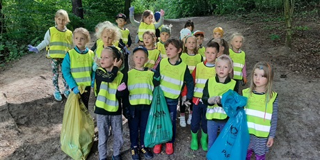 Powiększ grafikę: 6-latki w lesie stoją i pokazują zebrane śmieci