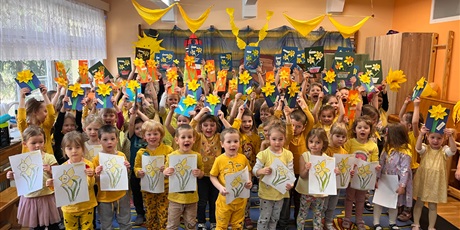 Powiększ grafikę: Przedszkolaki w żółtych strojach stoją i pokazują swoje prace plastyczne z żółtymi kwiatami.