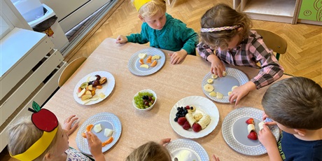 Powiększ grafikę: 5 dzieci ze Smykusiów przy stole układa sałatkę z owoców na talerzykach