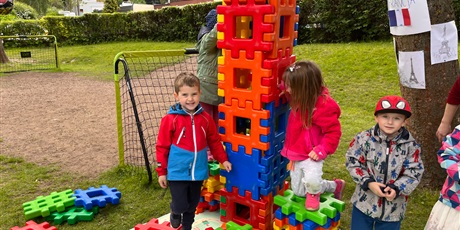 Powiększ grafikę: Troje dzieci buduje z dużych klocków w ogrodzie