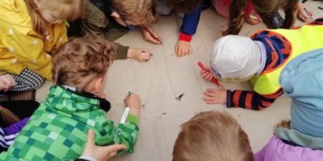 Powiększ grafikę: Grupa dzieci rysuje wspólną pracę plastyczną w ogrodzie